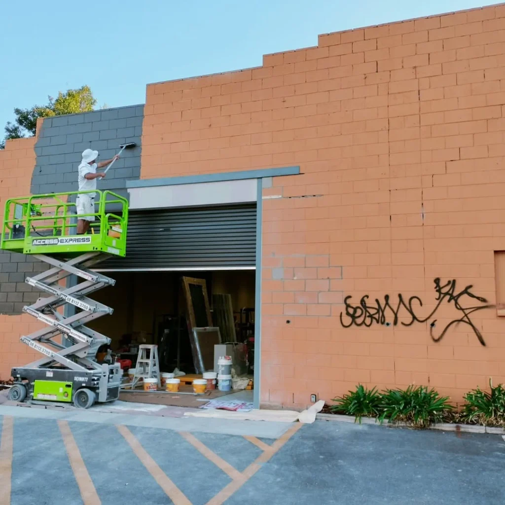 Professional painters spraying and rolling paint on a commercial exterior wall in Adelaide